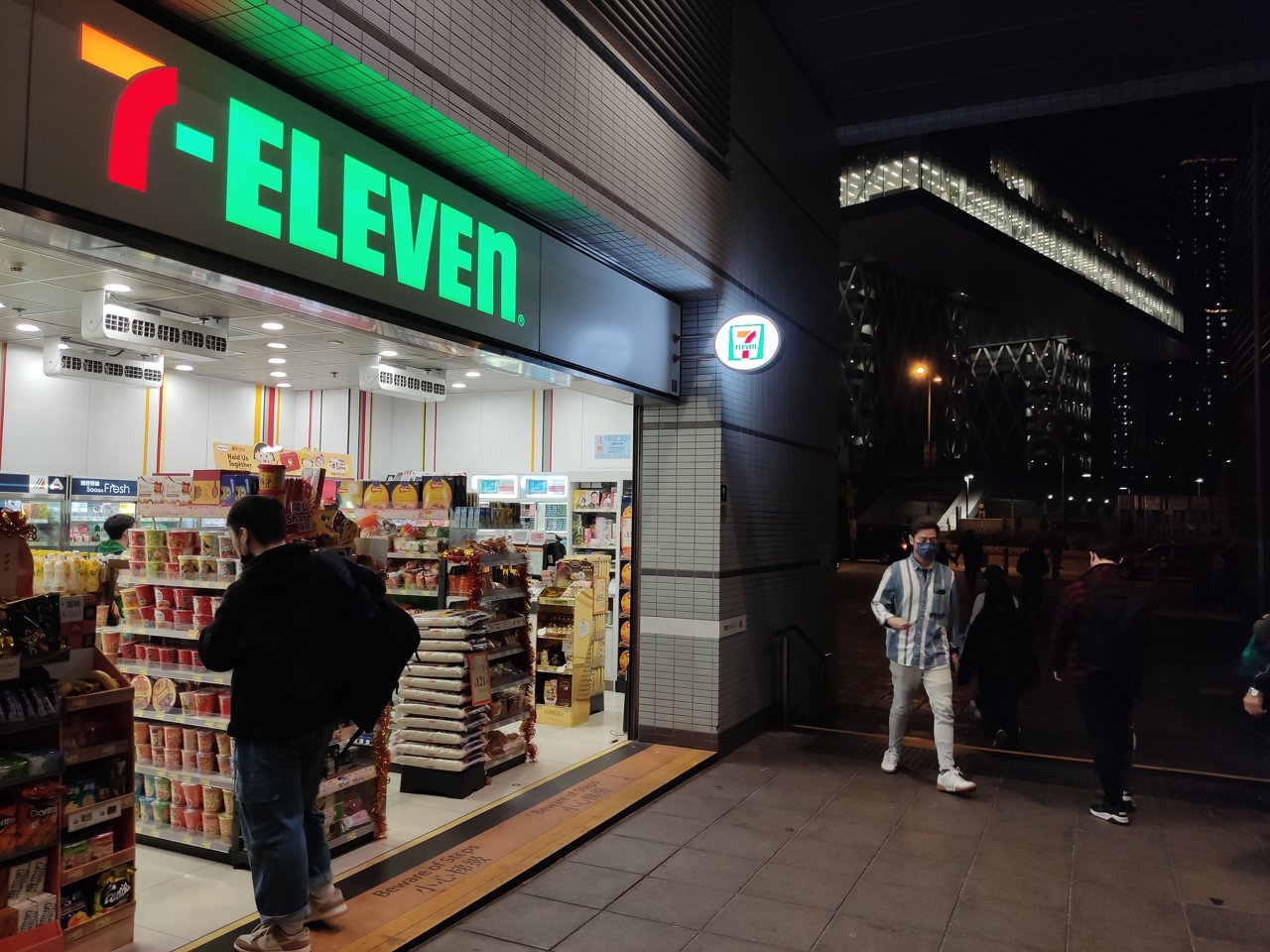 Night-time 7-Eleven shop entrance with illuminated signage at Tiu Keng Leng station. Historic brand reference, not the Mong Kok recording.